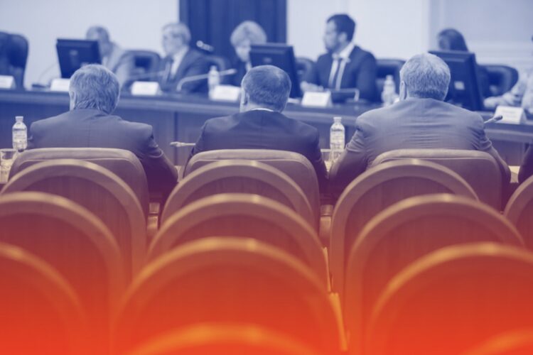 Drie mannen in pak zittend en luisterend in een overheidsgebouw